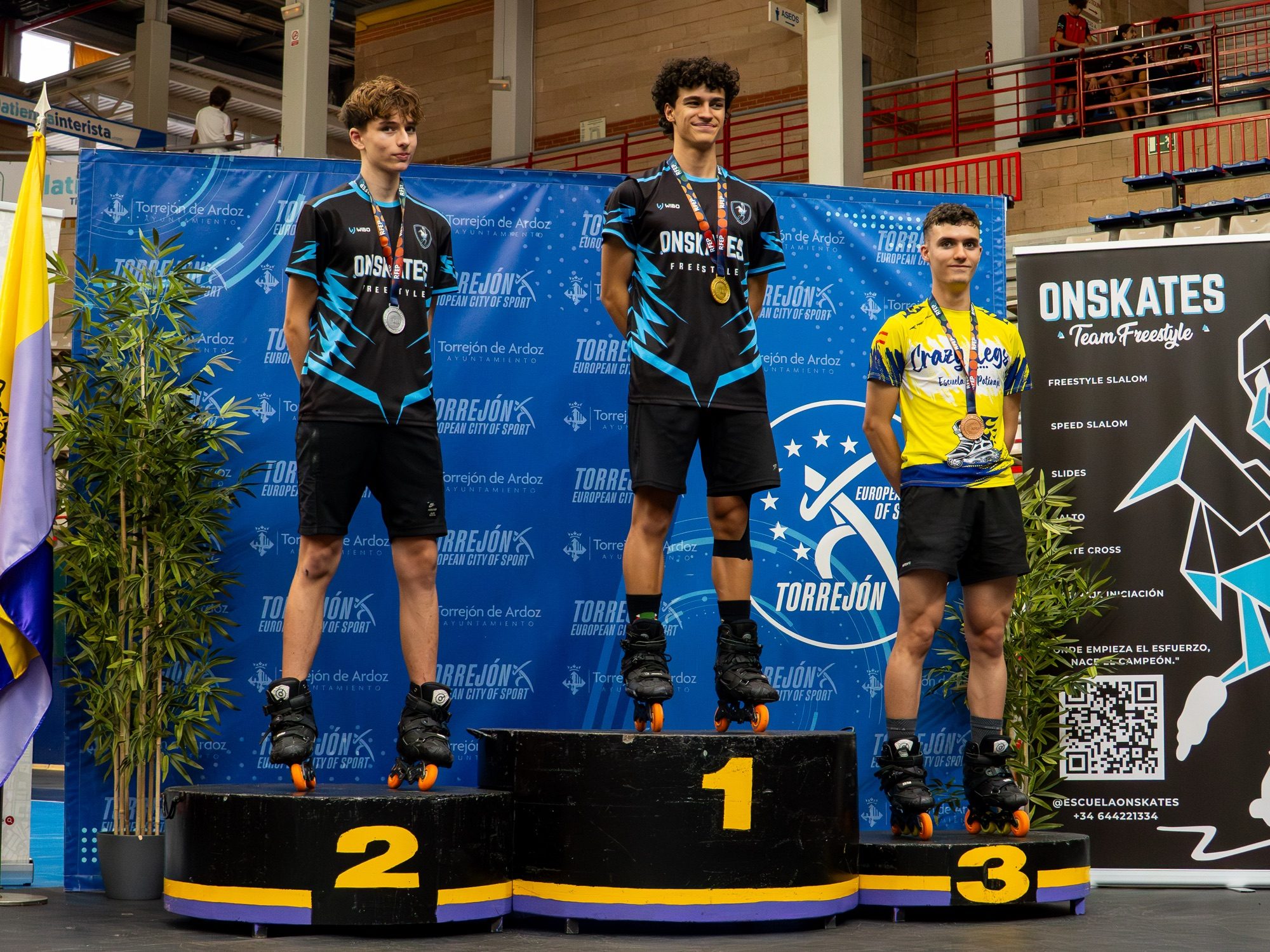 Dos patinadores del Team Onskates en el podio del Campeonato de España, oro y plata, con el roll-up del club al fondo