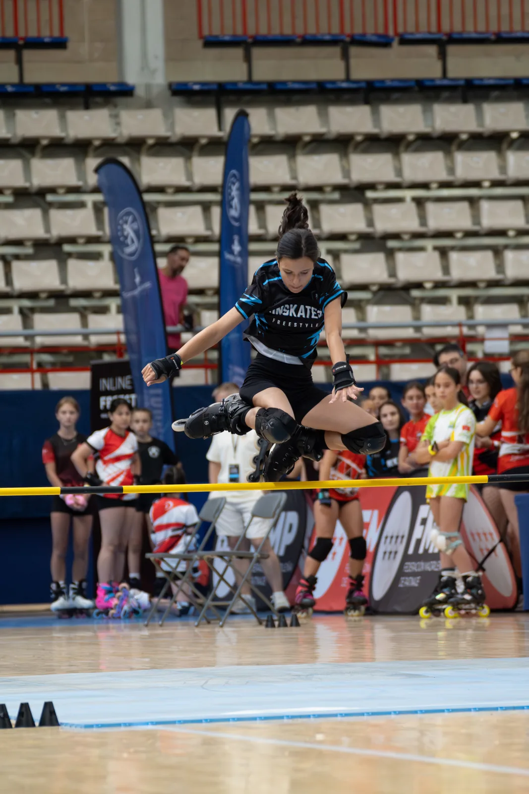 Patinadora del Team Onskates saltando una valla en plena competición, con público al fondo